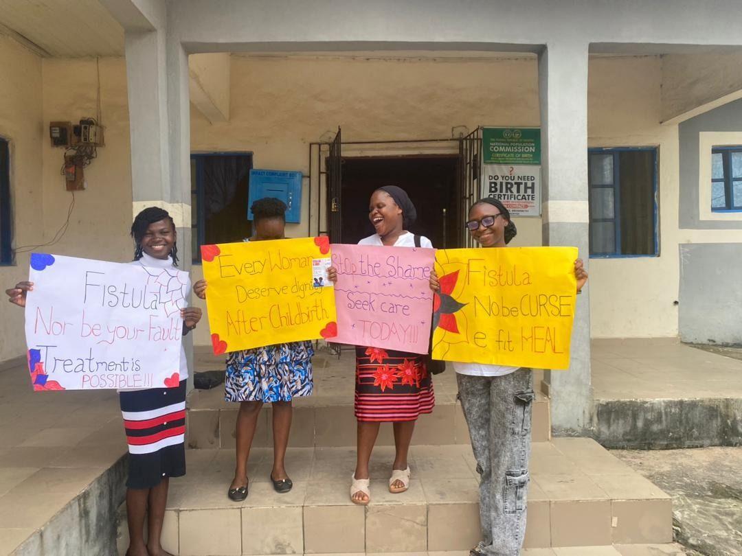 Four FCI volunteers outside a health centre hold signs saying fistula is not your fault and treatment is possible