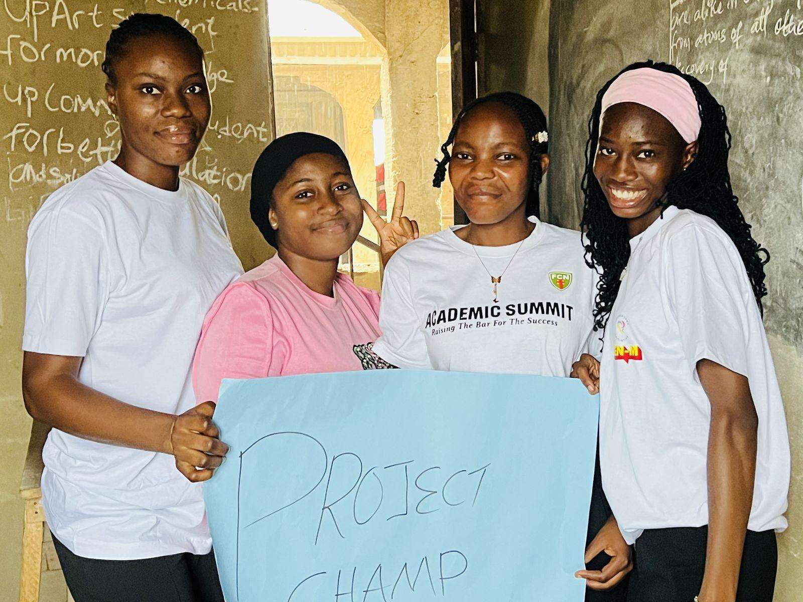 Four smiling FCI volunteers hold a hand-lettered Project Champ sign in a school classroom